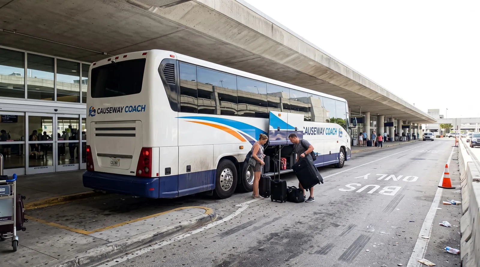 Travellers with suitcases at the open luggage bay of a Causeway Coach motorcoach on the departures kerb at Miami International