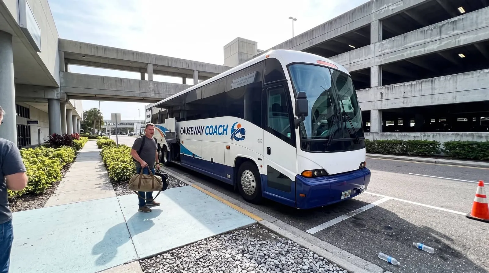 A traveller with a duffel bag at the open luggage bay of a Causeway Coach motorcoach outside Tampa International Airport